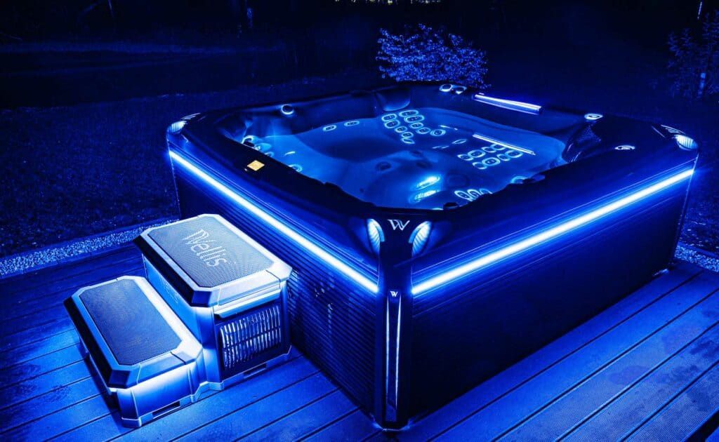 A blue-lit hot tub on a deck at night, with illuminated steps.