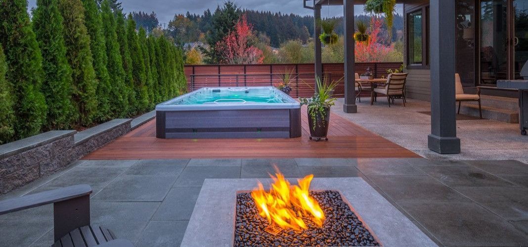 Backyard patio with a hot tub, fire pit, and seating area. Overcast sky with fall colors.