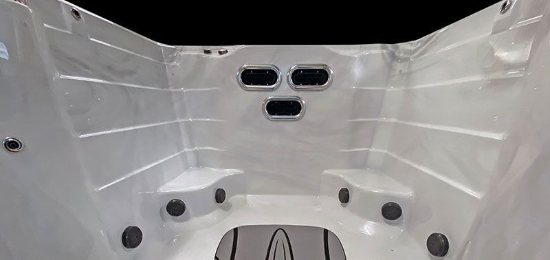 Interior of a white hot tub with seats, jets, and a black panel.