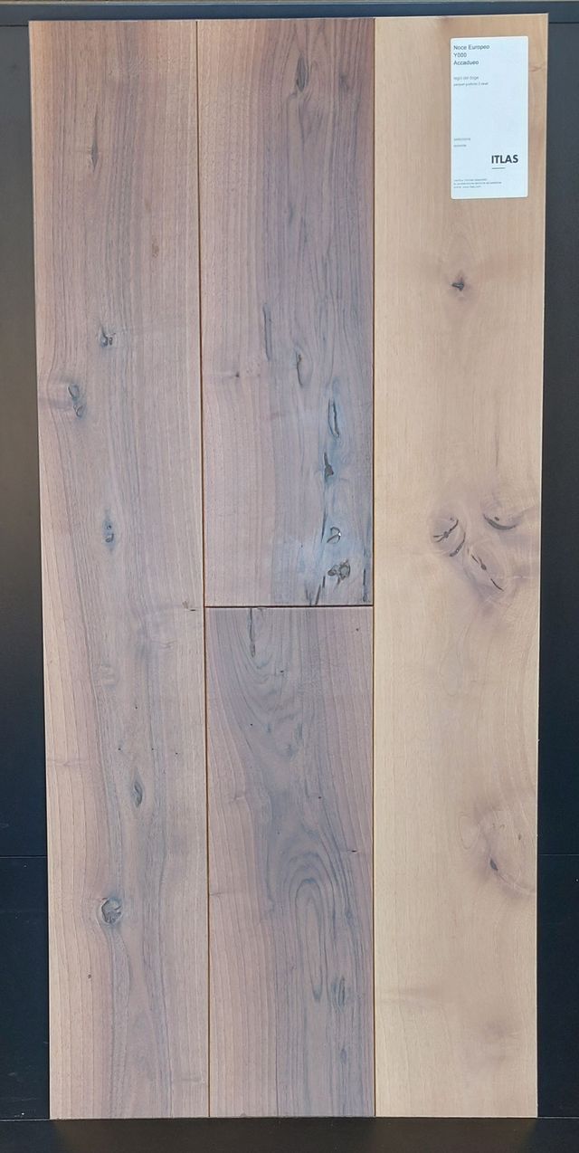 Tre assi di legno, due di tonalità più scura e una più chiara, con etichetta. Le assi sono strutturate e mostrano le venature del legno.