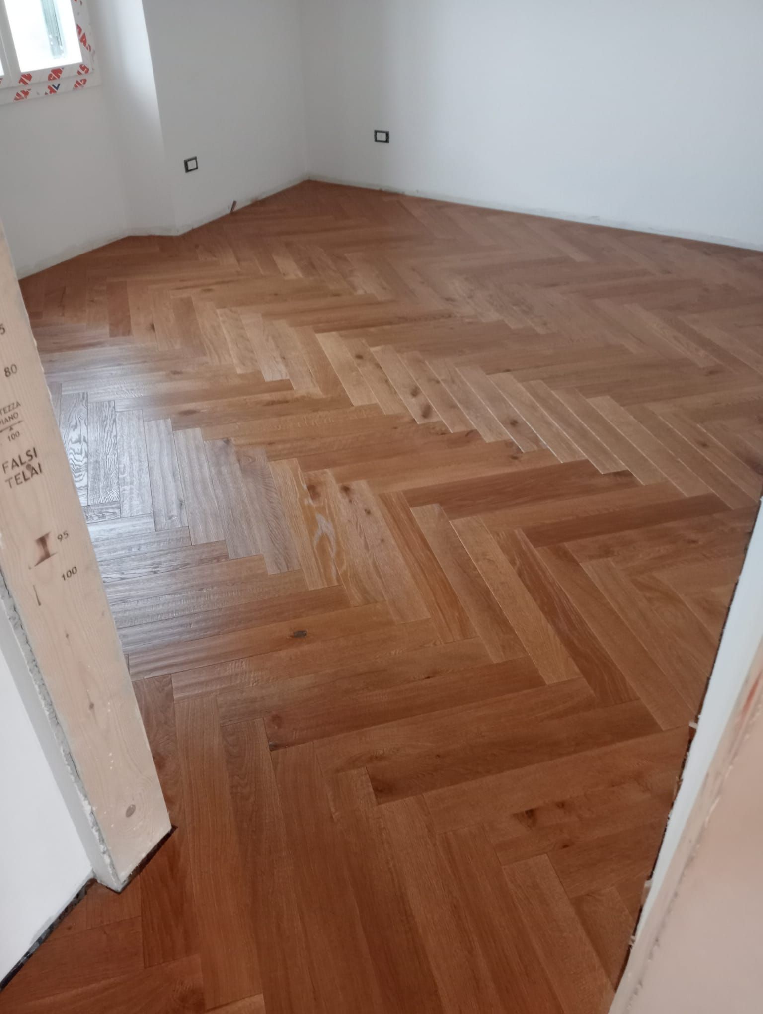 Pavimento in parquet a spina di pesce, appena installato in una stanza con pareti bianche.