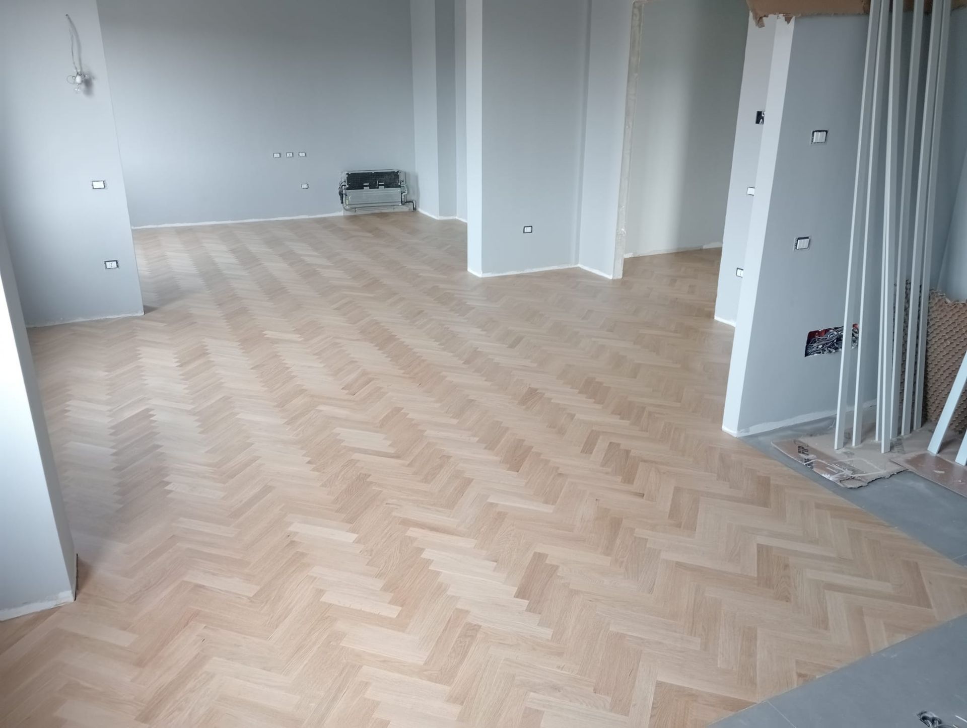 Pavimento a spina di pesce in legno chiaro in una stanza con pareti grigie.