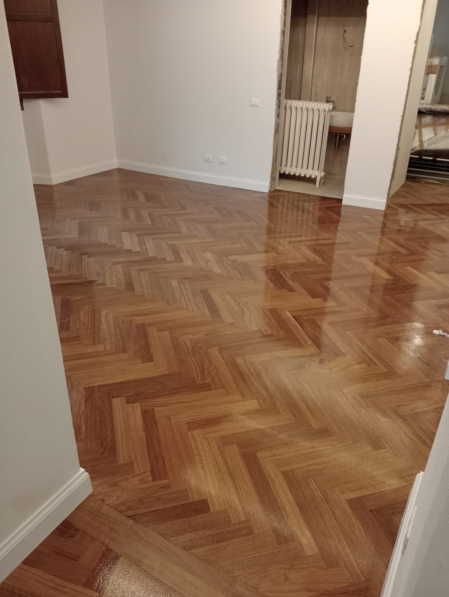 Una stanza con pavimento in parquet lucido disposto a spina di pesce; pareti e finiture bianche.