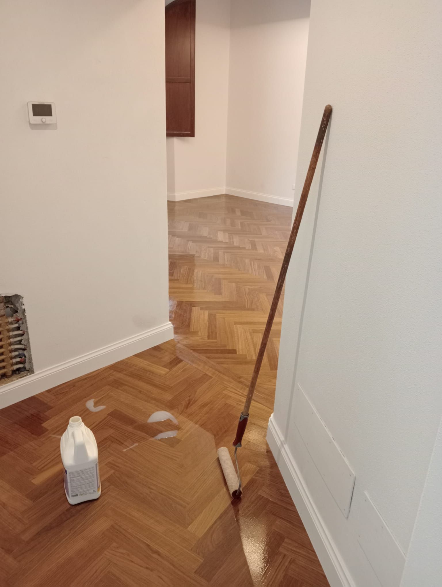 Un pavimento in legno è in fase di rifinitura; sul pavimento ci sono un rullo e una bottiglia di detergente.