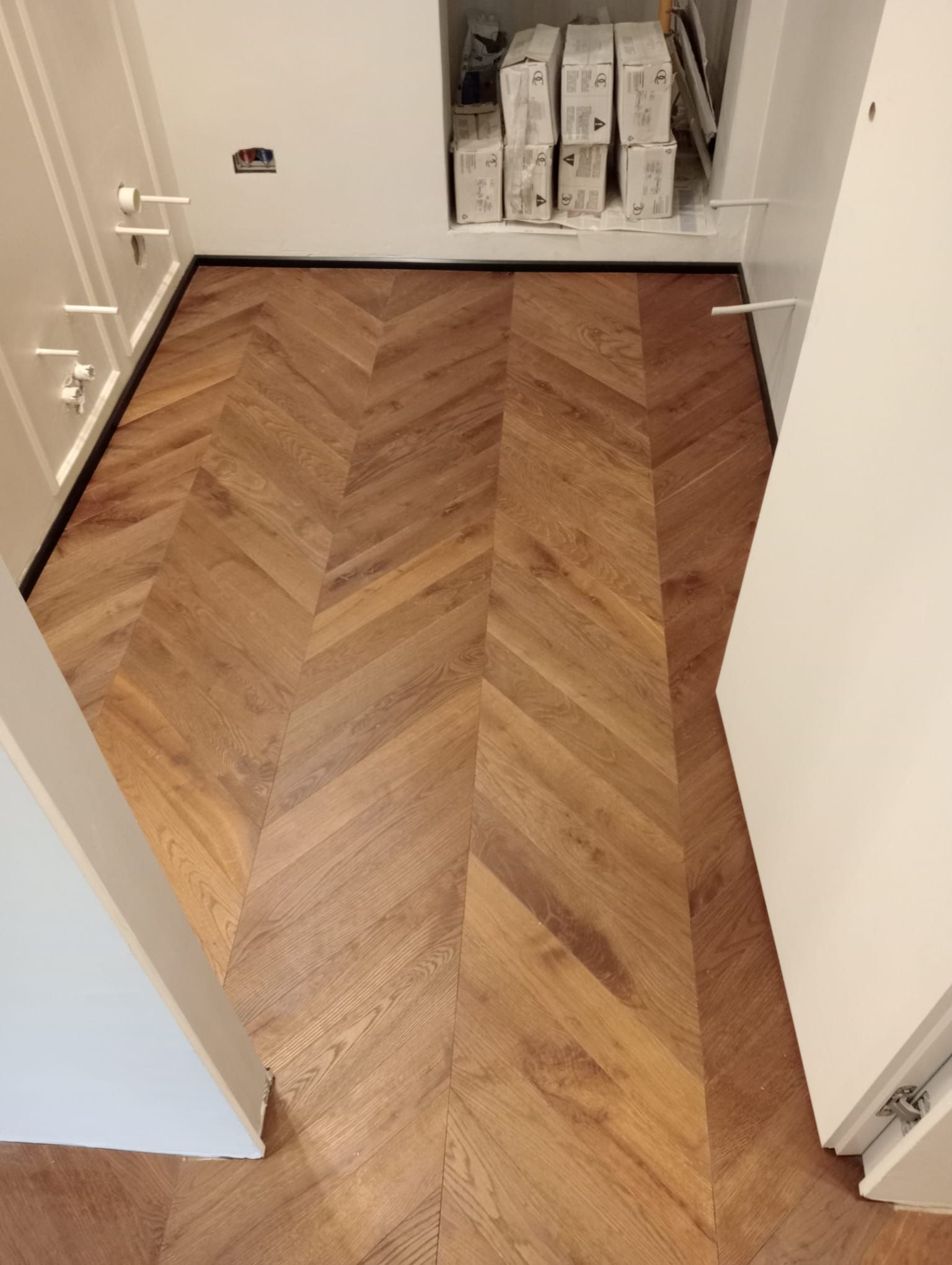 Pavimento in legno a spina di pesce tra armadi bianchi.