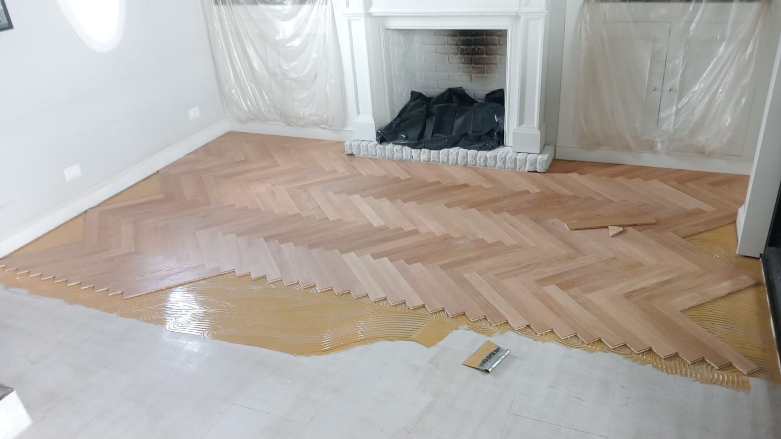 Installazione di un pavimento in parquet in una stanza. La colla viene stesa sul sottofondo e i pezzi di legno vengono posati a spina di pesce.