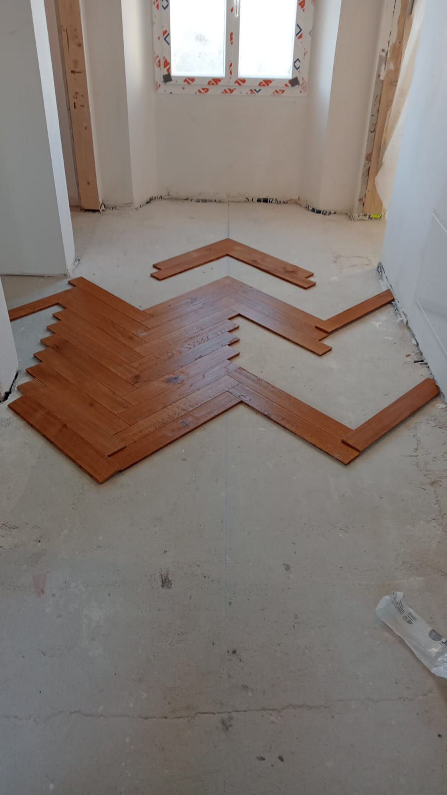 Pavimento in parquet in una stanza con una finestra sullo sfondo. Le assi sono disposte a spina di pesce.