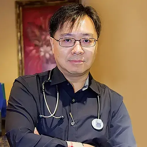 A man wearing glasses and a stethoscope is standing with his arms crossed.