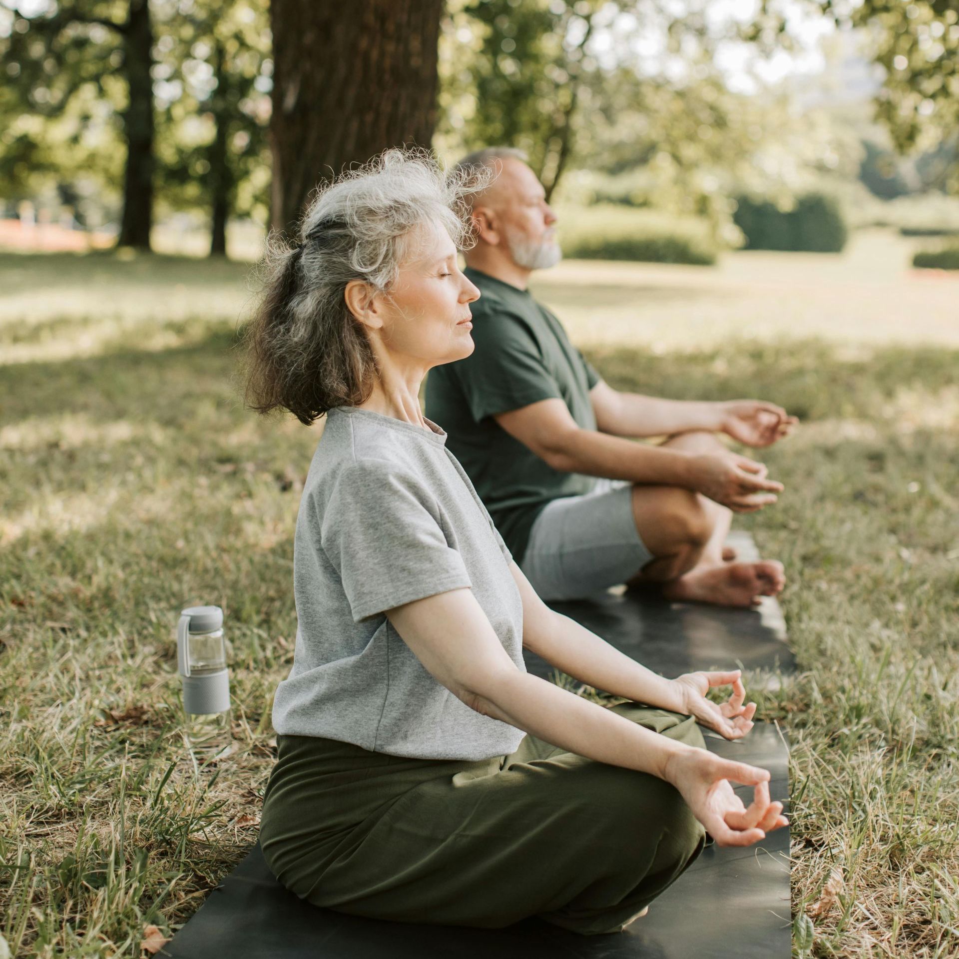 A man and a woman are sitting on yoga mats in a park.