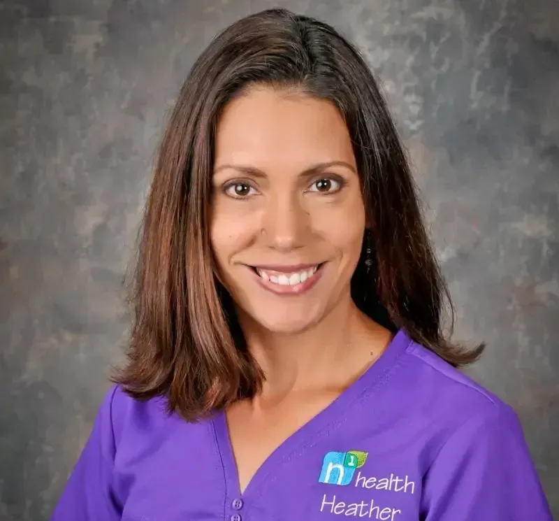 A smiling woman wearing a purple health heather scrub top