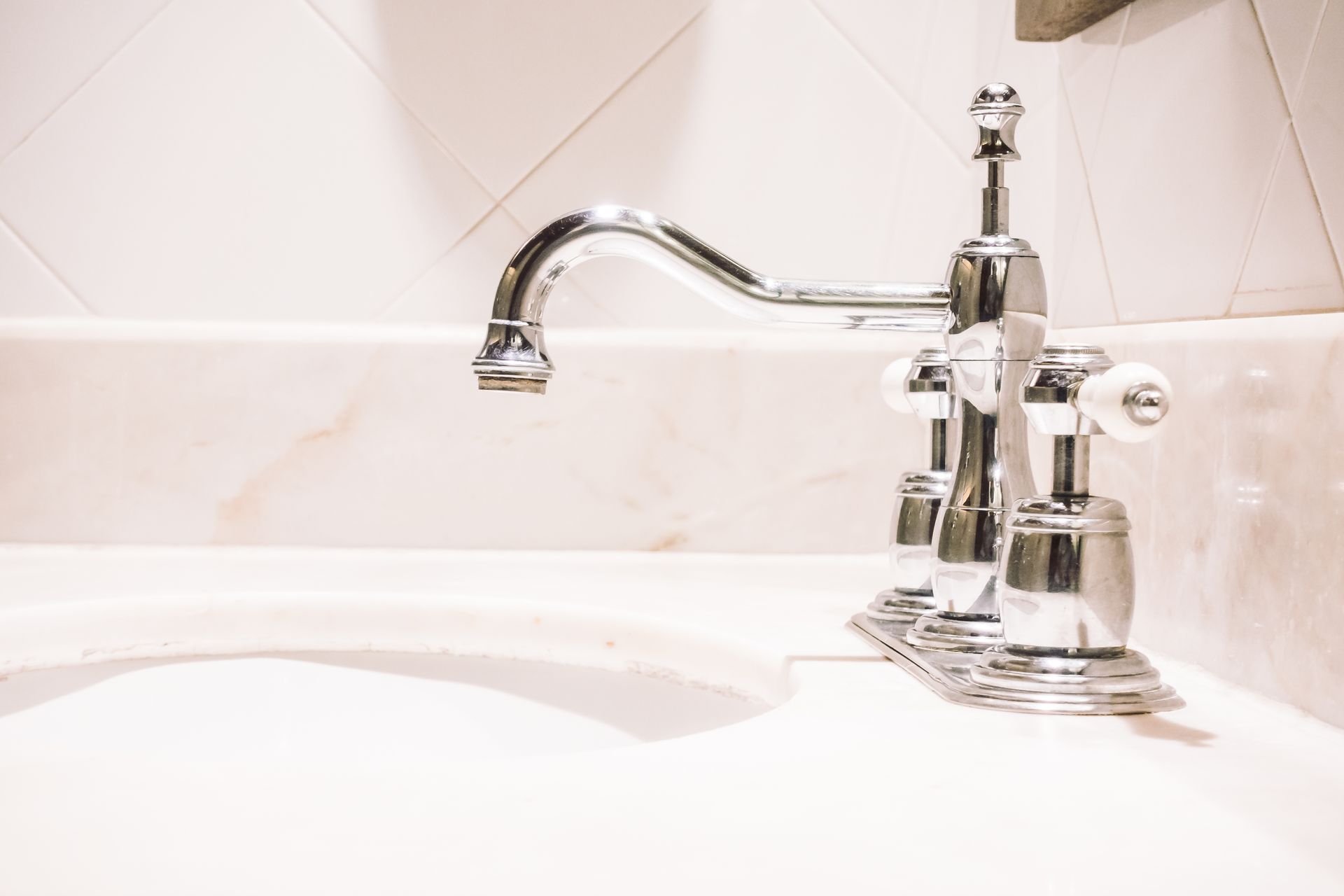 Shiny chrome faucet over a white sink, set against a white tiled wall.