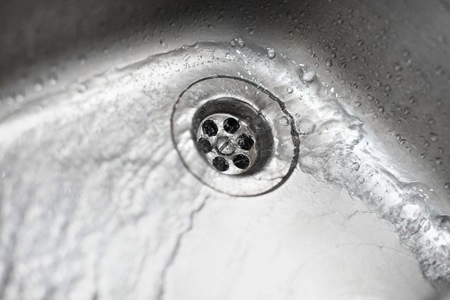 Water flowing into a stainless steel sink, over and around a drain.