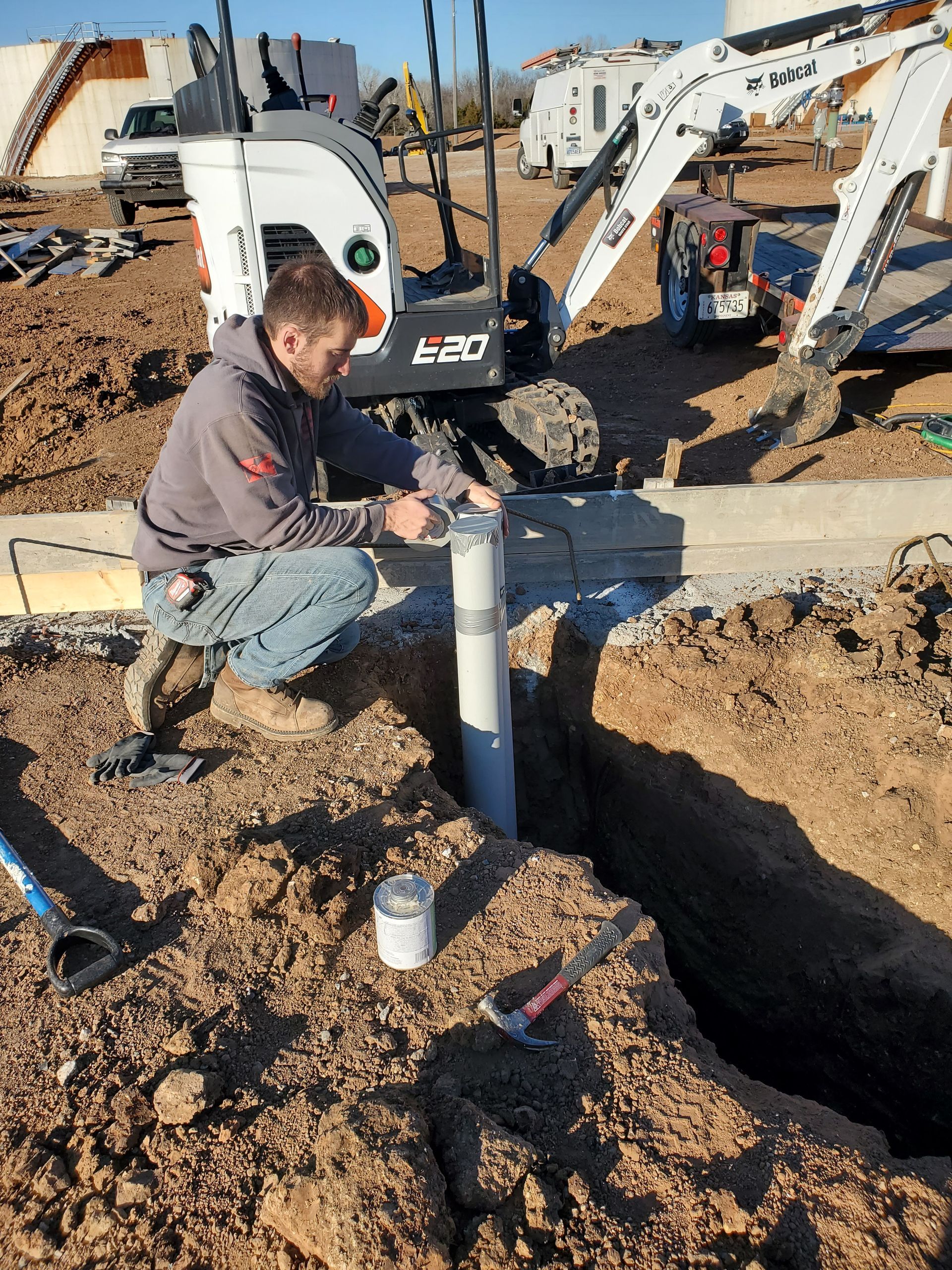 A man is kneeling in the dirt working on a pipe.