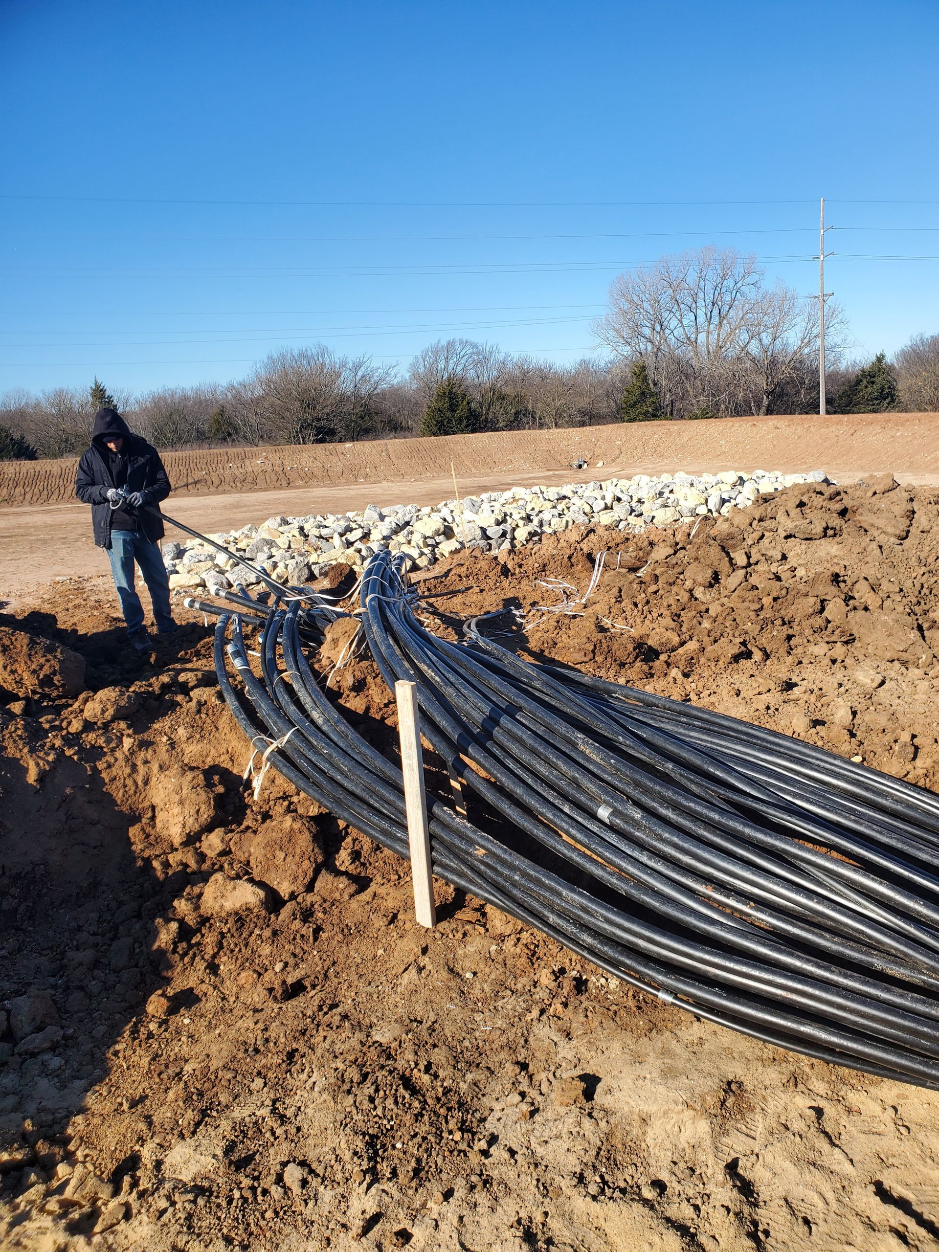 A man is standing next to a pile of pipes in the dirt.