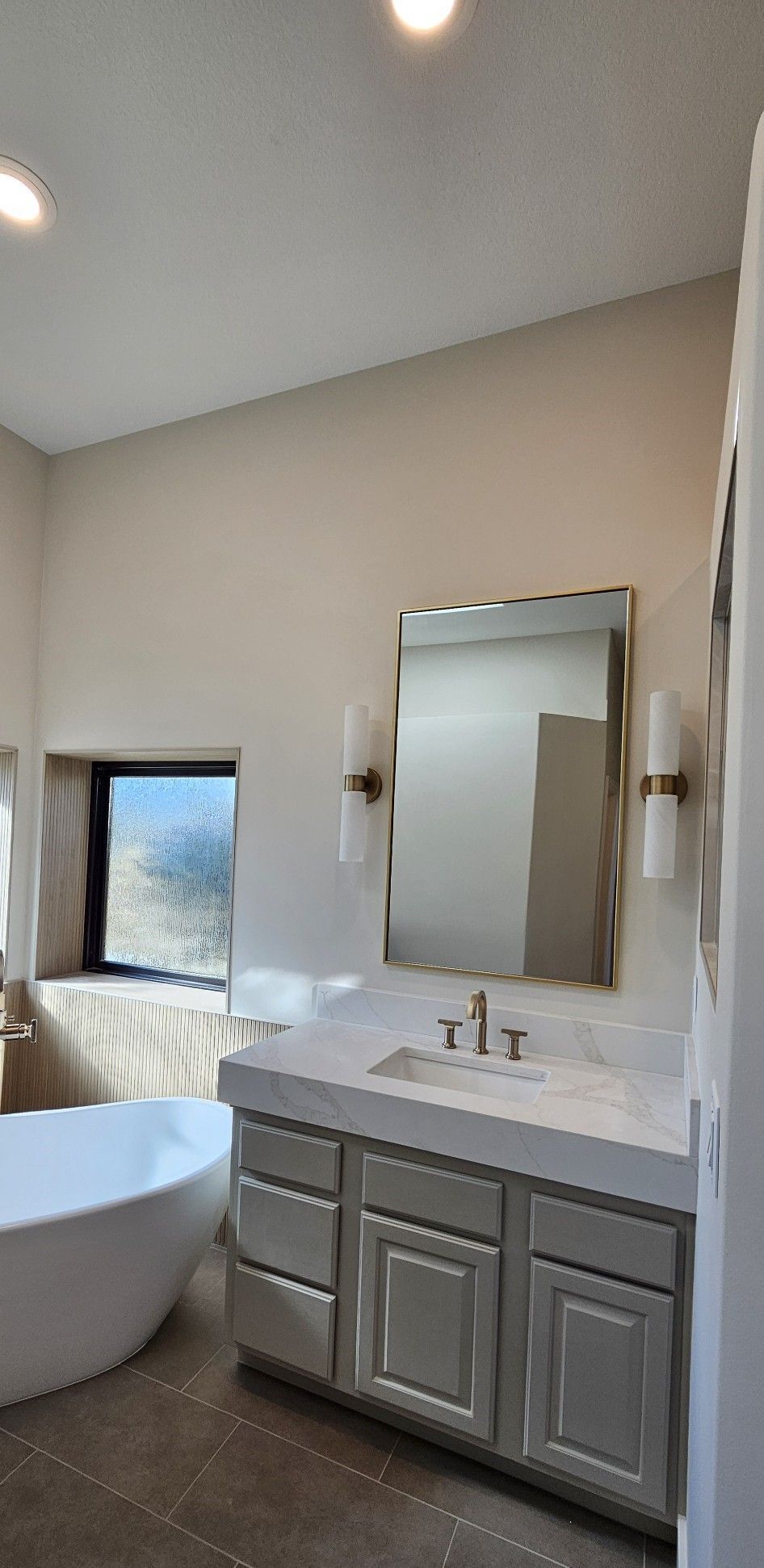 Bathroom with freestanding tub, gray vanity, large mirror, and window.