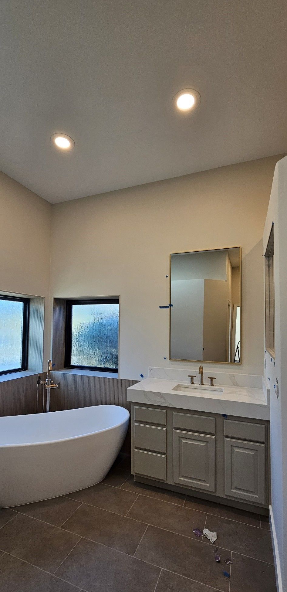 Modern bathroom with a bathtub, vanity, and large mirror; neutral tones and natural light.