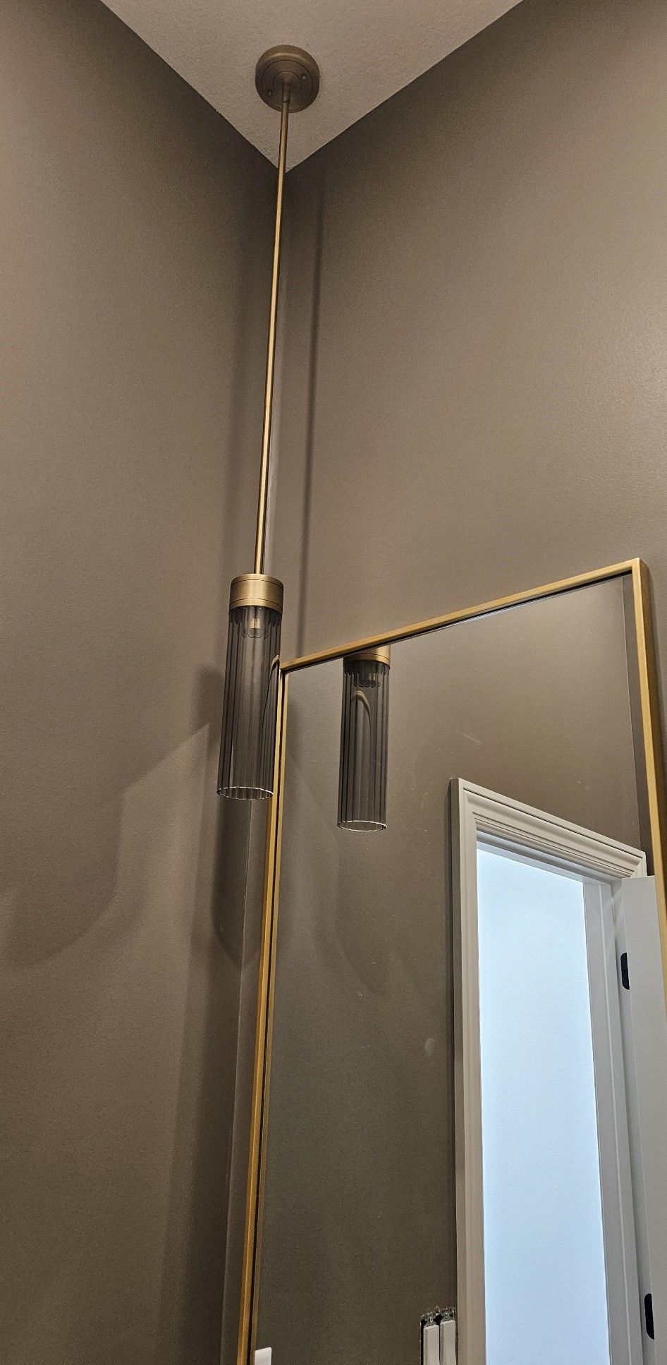 A modern hanging light fixture in a bathroom with a large mirror.