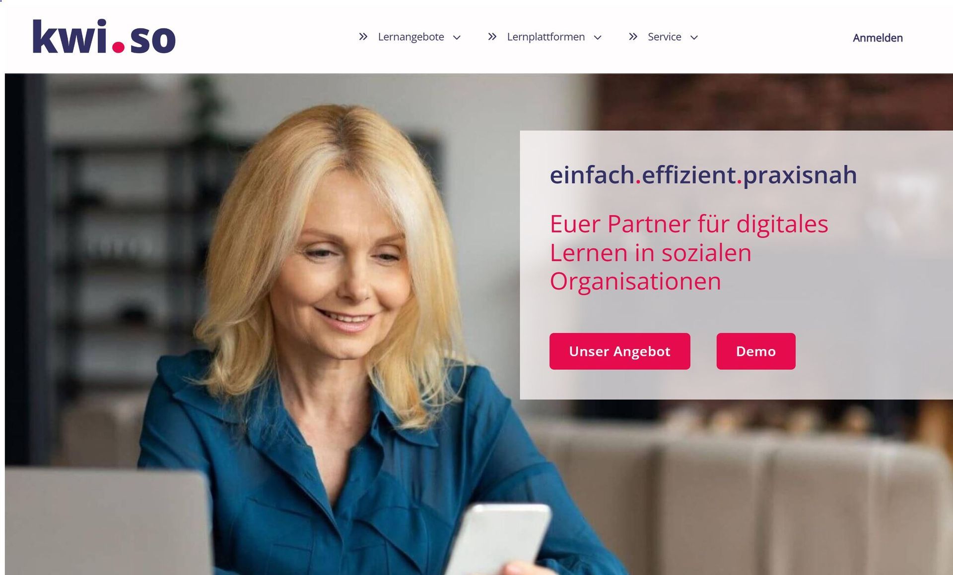 Eine Frau sitzt vor einem Laptop und hält ein Mobiltelefon in der Hand.