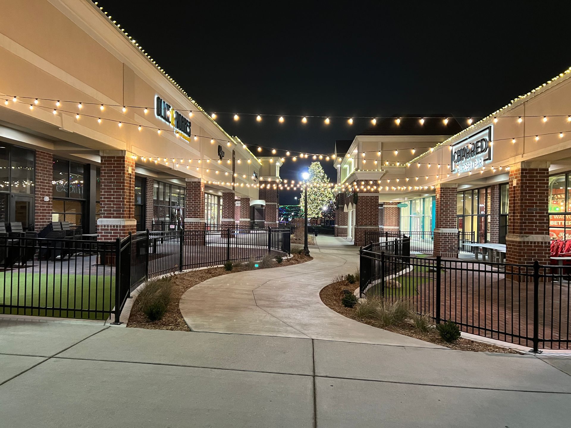 String lights over a curved walkway between lit storefronts at night.