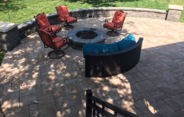 Outdoor stone patio with red chairs around a circular fire pit and blue curved bench seating