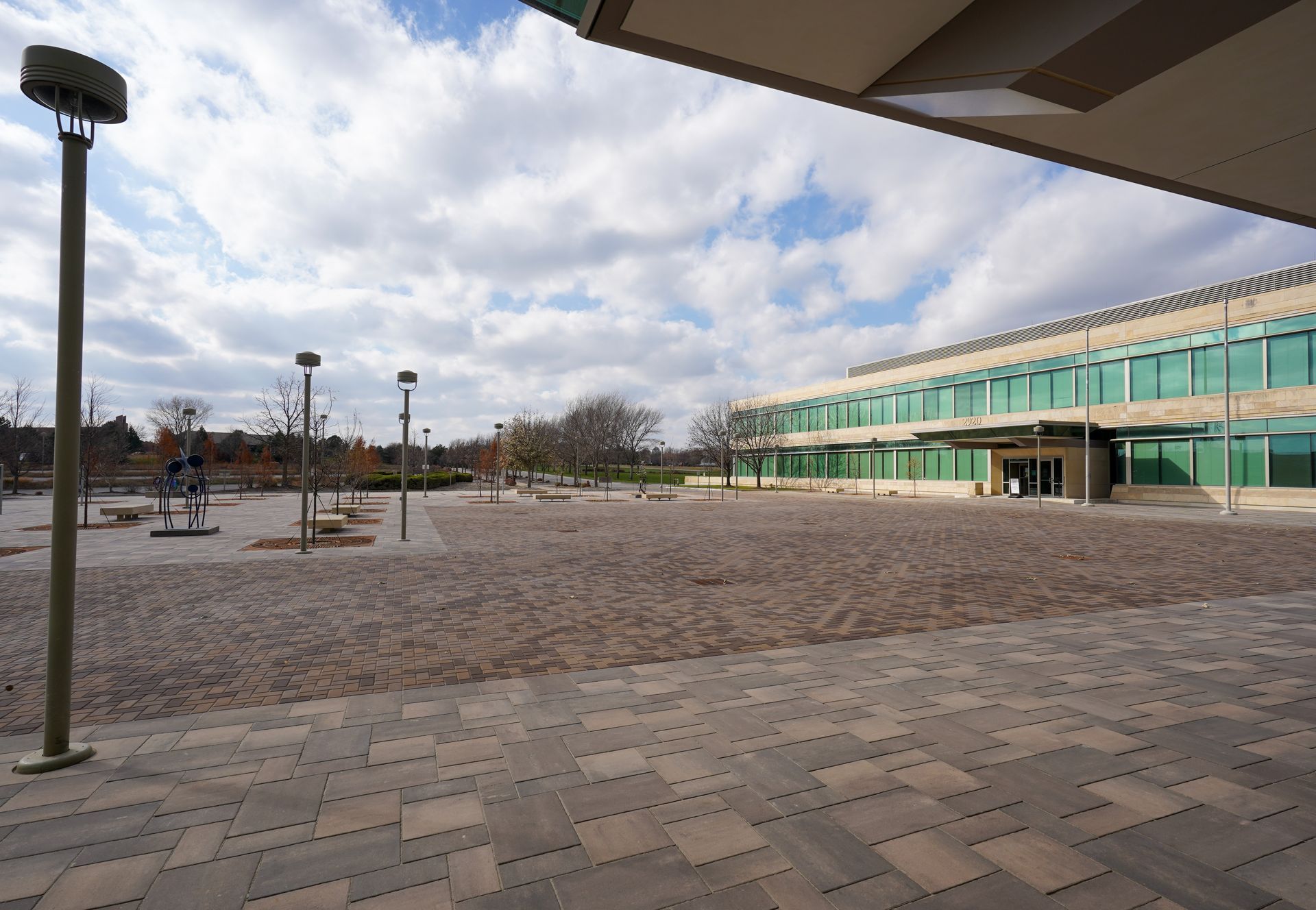 Empty outdoor plaza beside a modern green glass building under a cloudy sky