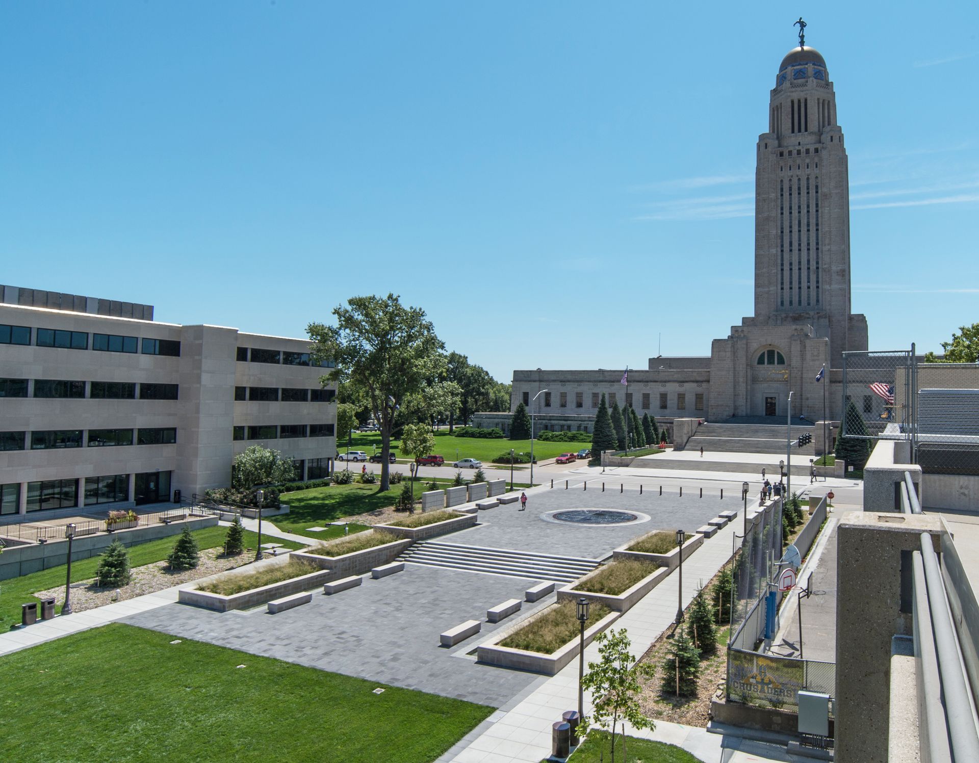 Modern government plaza with landscaping and a tall stone tower under a clear blue sky