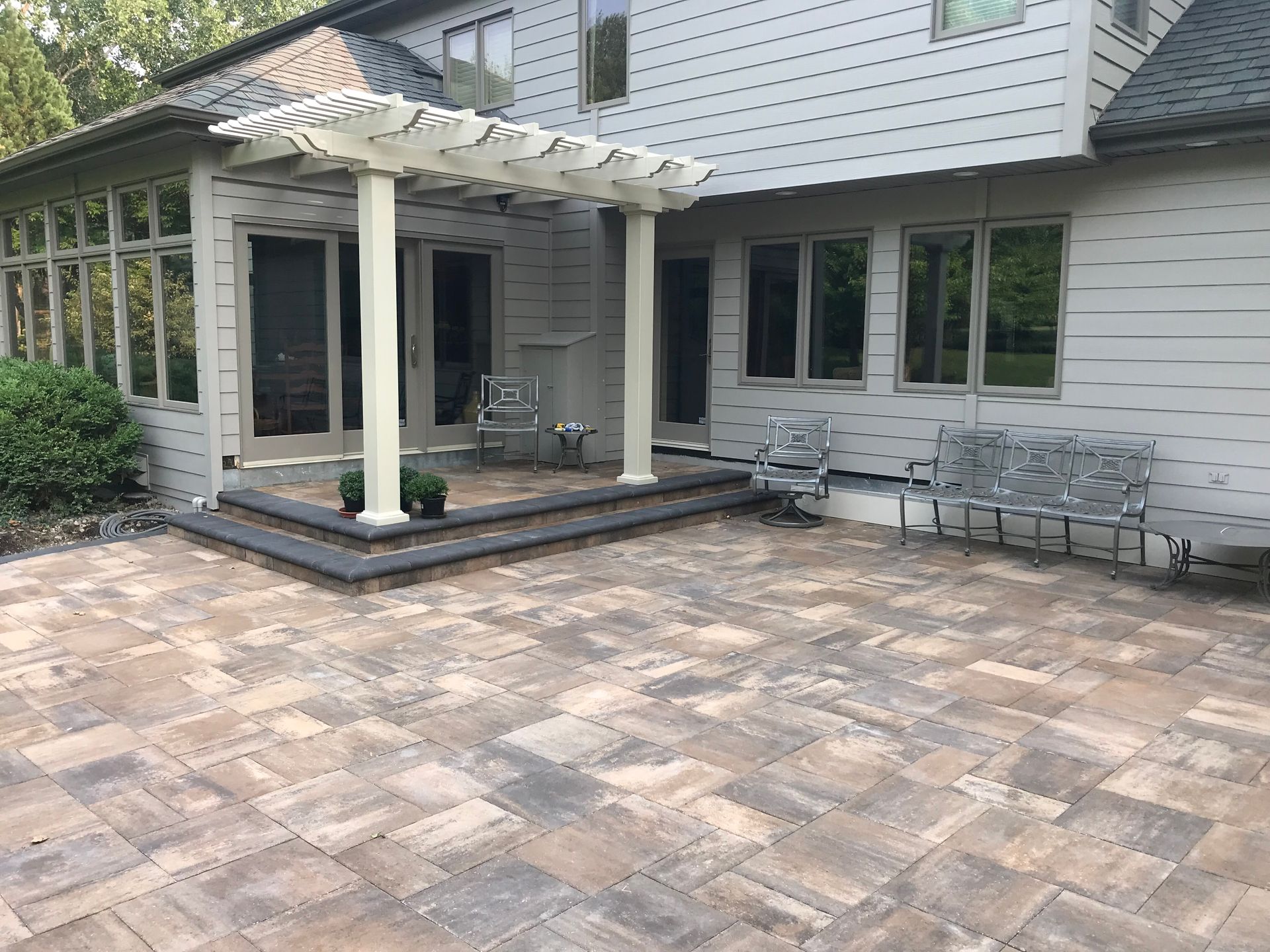 Patio with stone pavers, white pergola, and house exterior with sliding doors and windows
