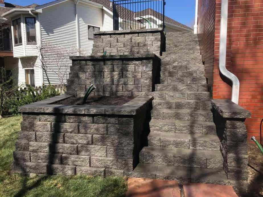 Stone outdoor staircase with retaining walls beside a house, featuring a curved white downspout.