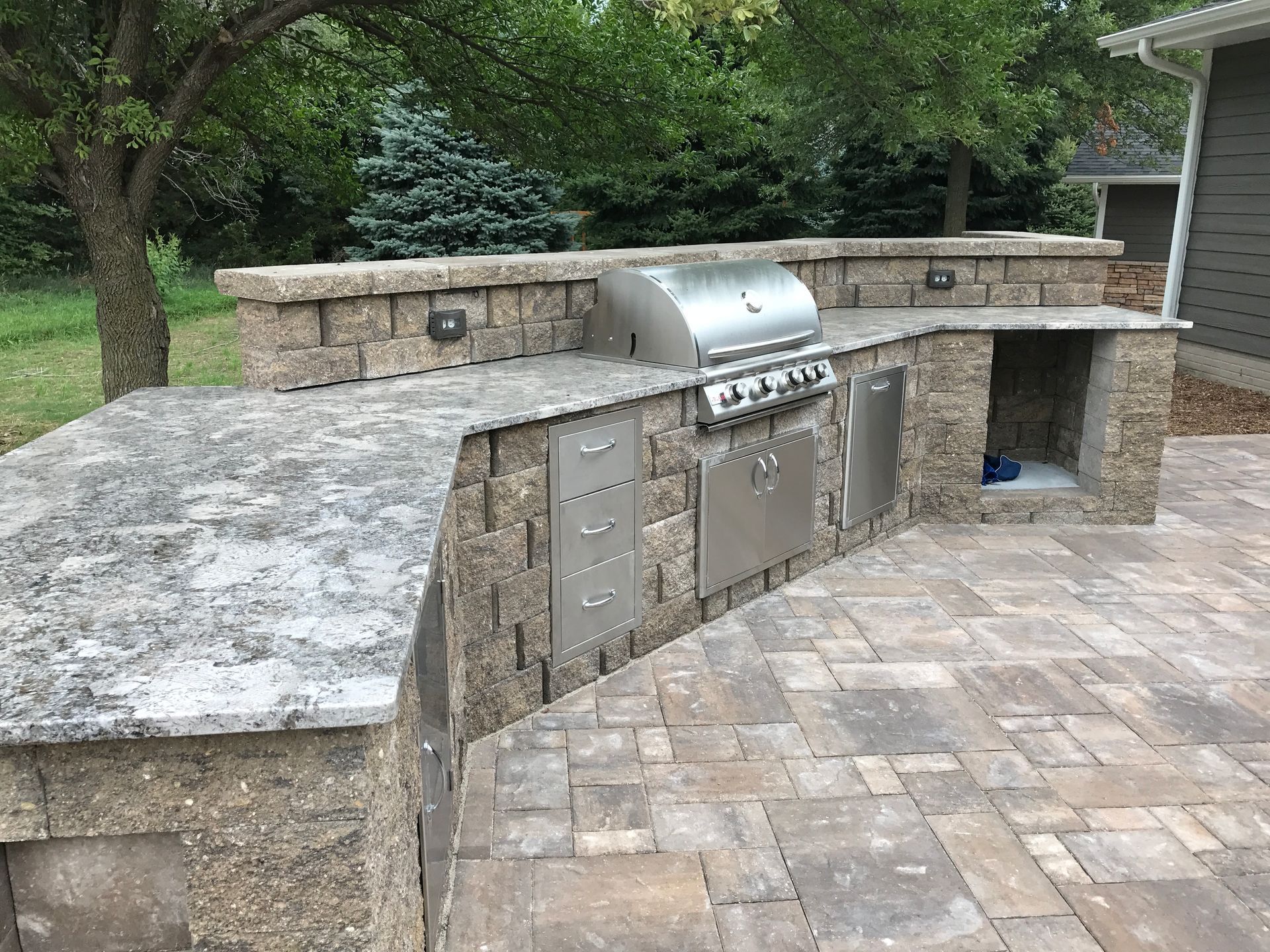 Outdoor stone patio with built-in stainless steel grill and counter under a stone wall walkway