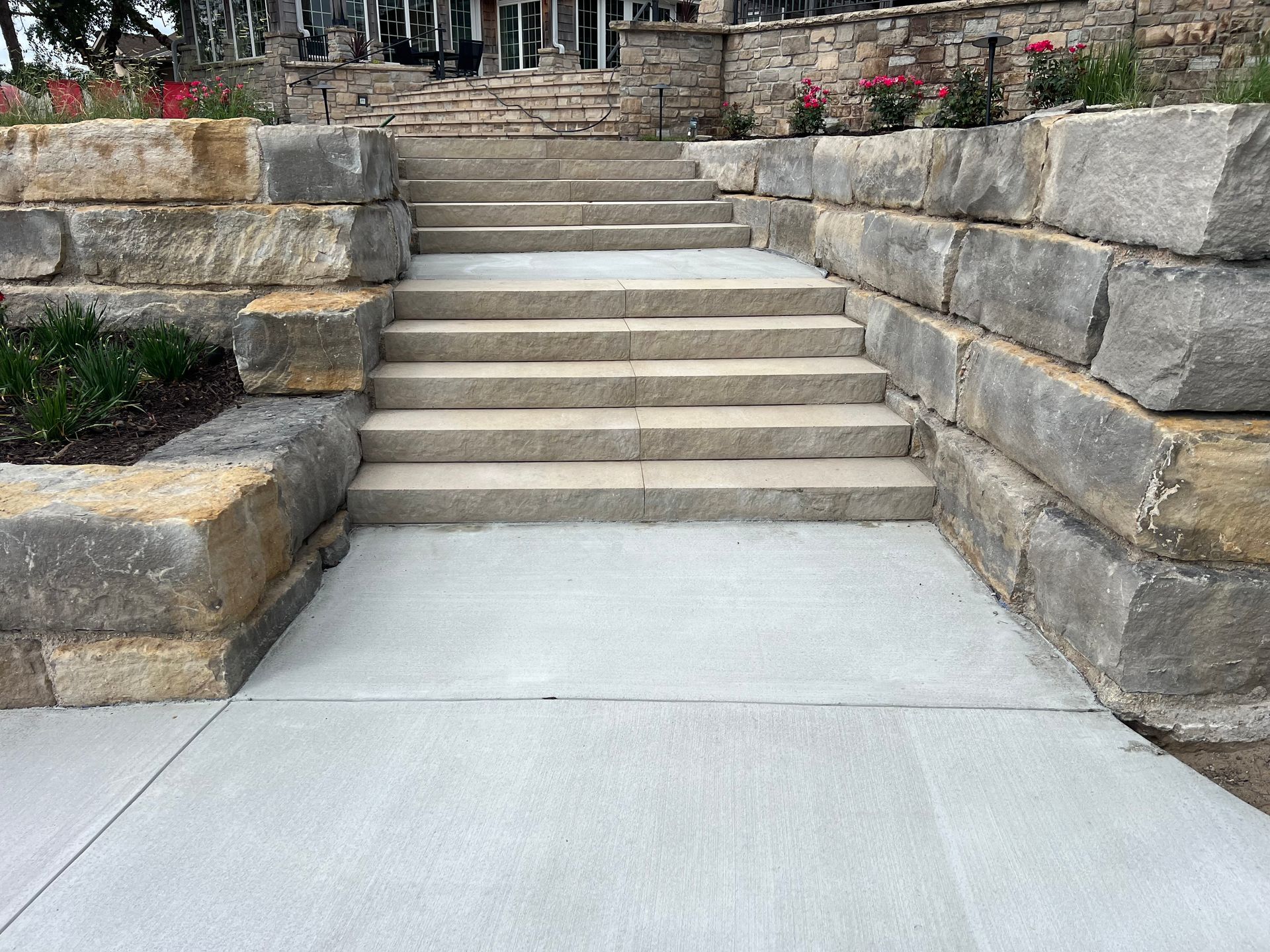 Concrete steps between stone retaining walls leading up to a garden path and building entrance