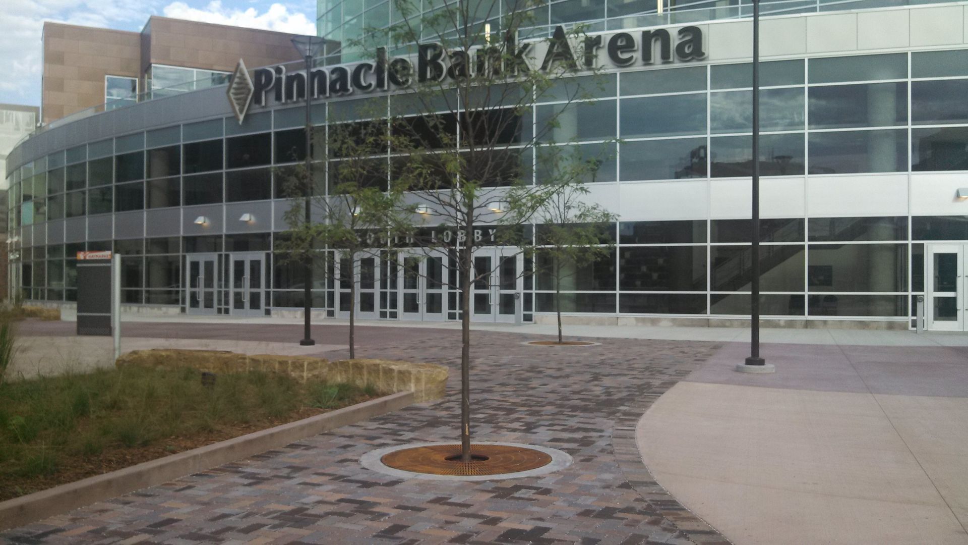 Exterior of Pinnacle Bank Arena, a glass-fronted building with curved facade and paved walkway.