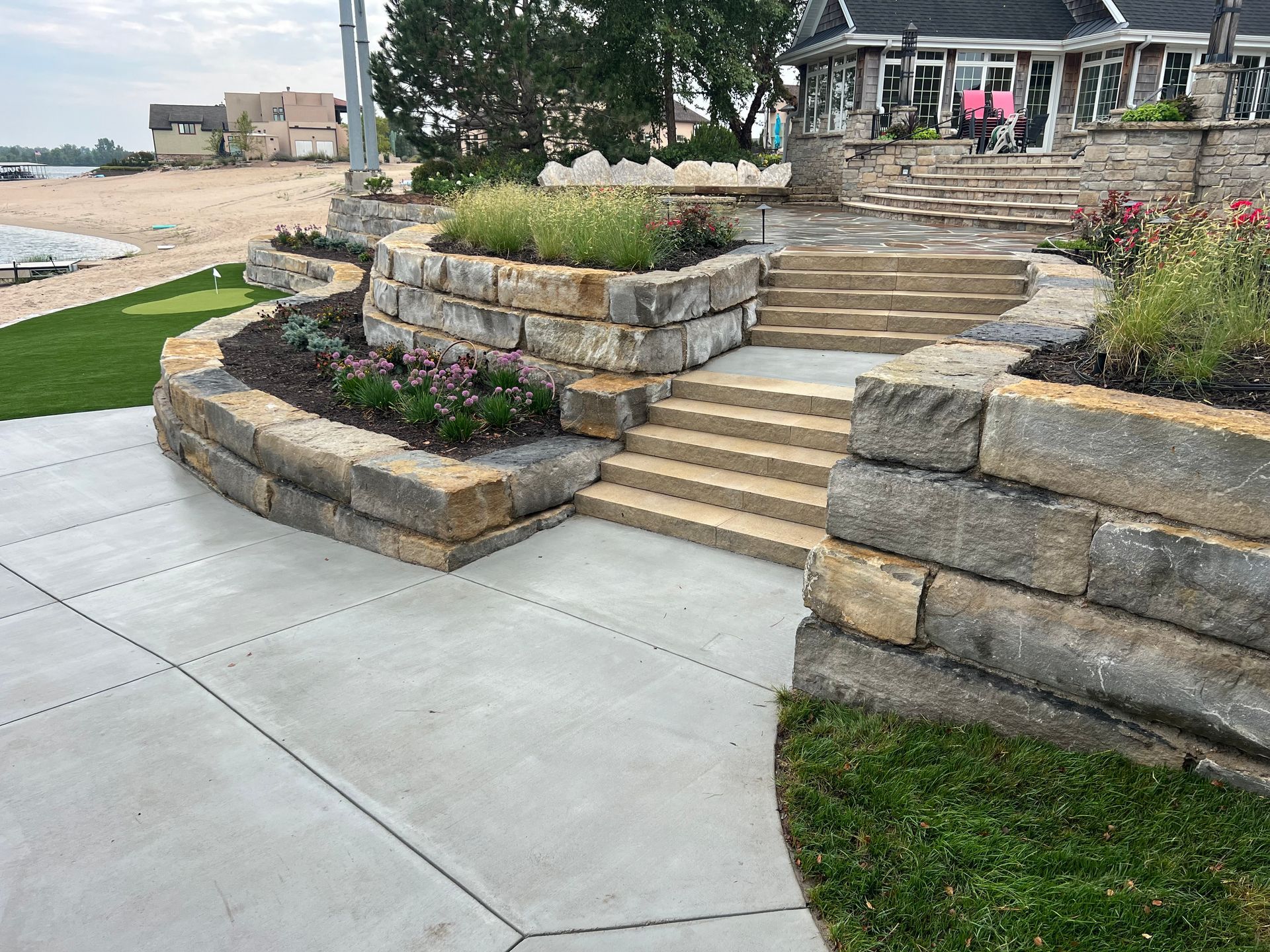 Landscaped stone steps and retaining walls beside a curved concrete walkway in a residential area