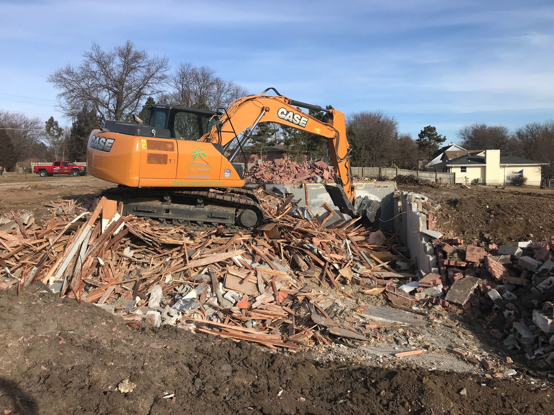 Orange excavator demolishing a brick structure amid rubble at a construction site.