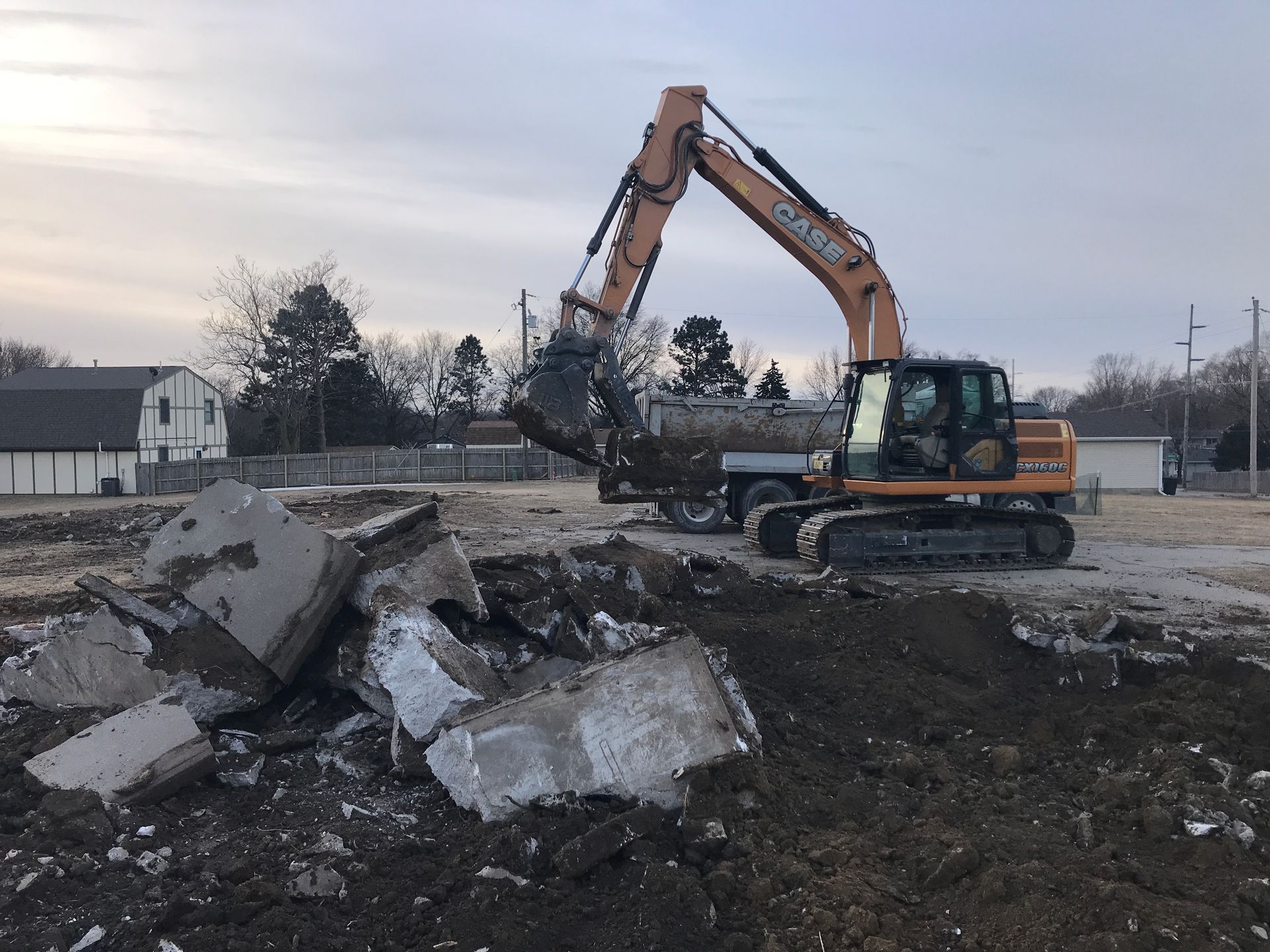 Orange excavator demolishing concrete debris on a construction site at dusk