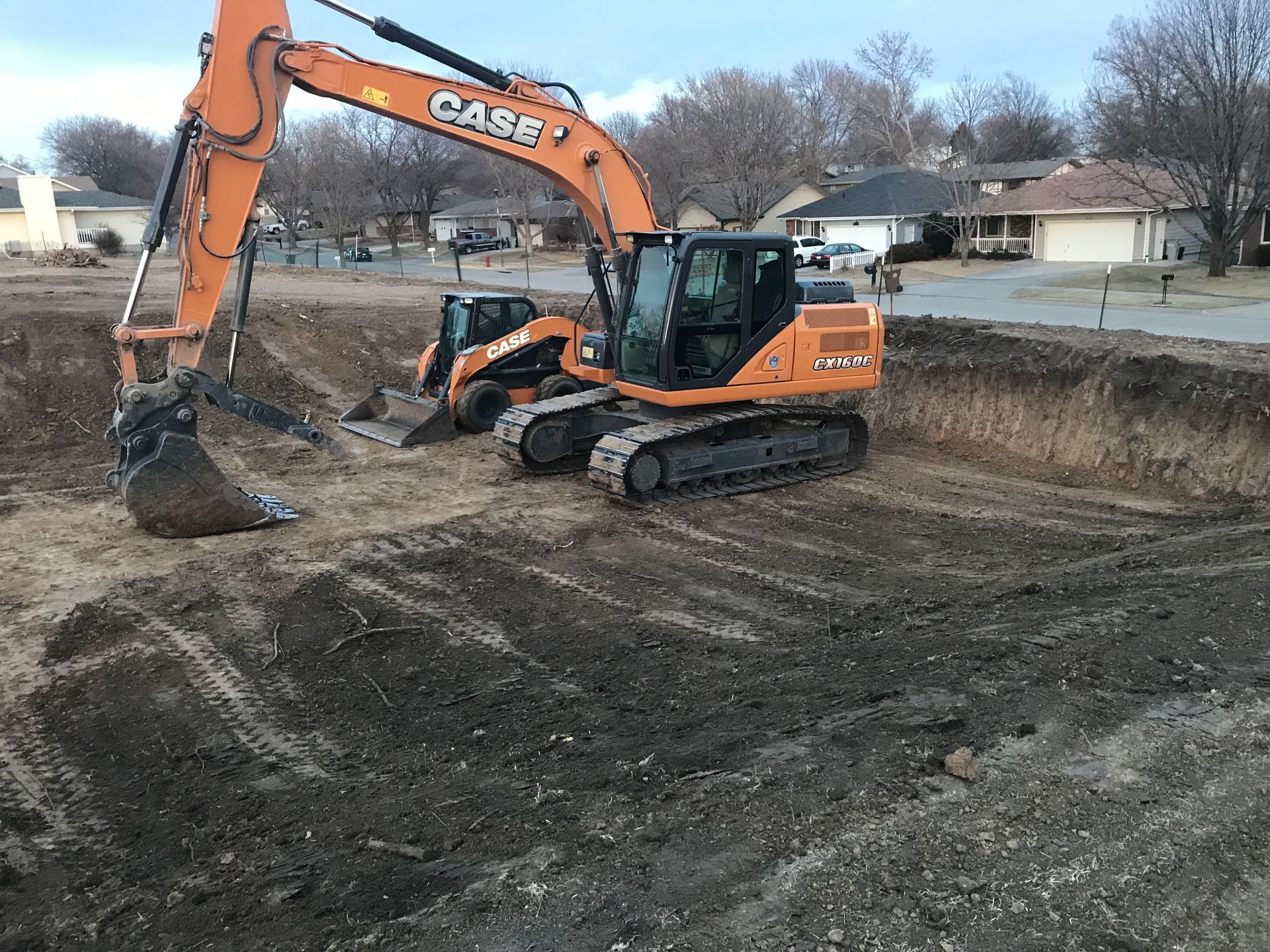 Orange excavator at a muddy construction site with a small tracked machine nearby