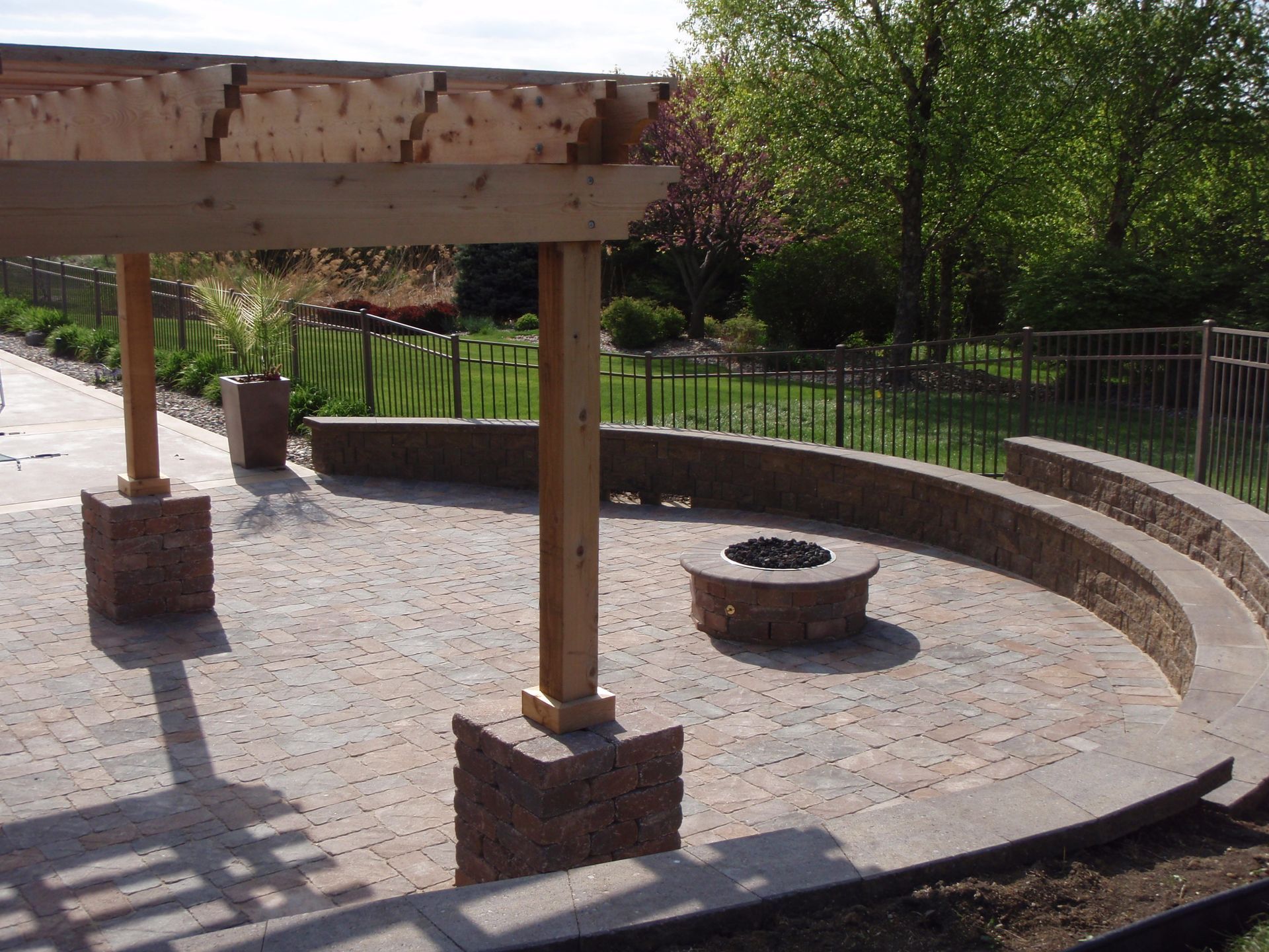 Curved stone fire pit with wooden pergola and benches in a sunny outdoor park area