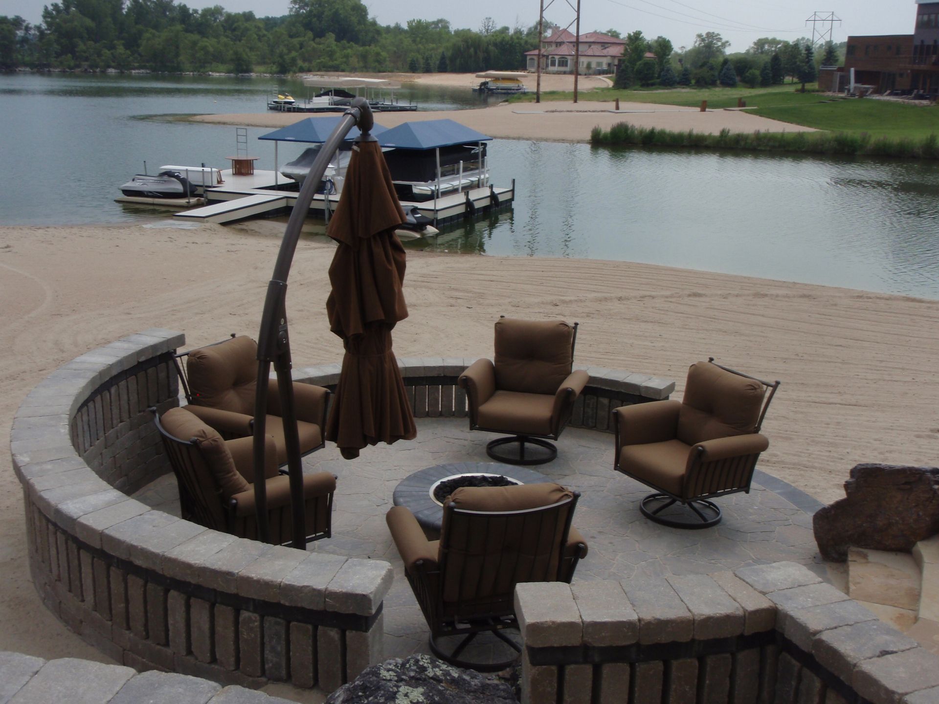 Lakeside patio with wicker chairs, closed umbrella, and boats docked on calm water