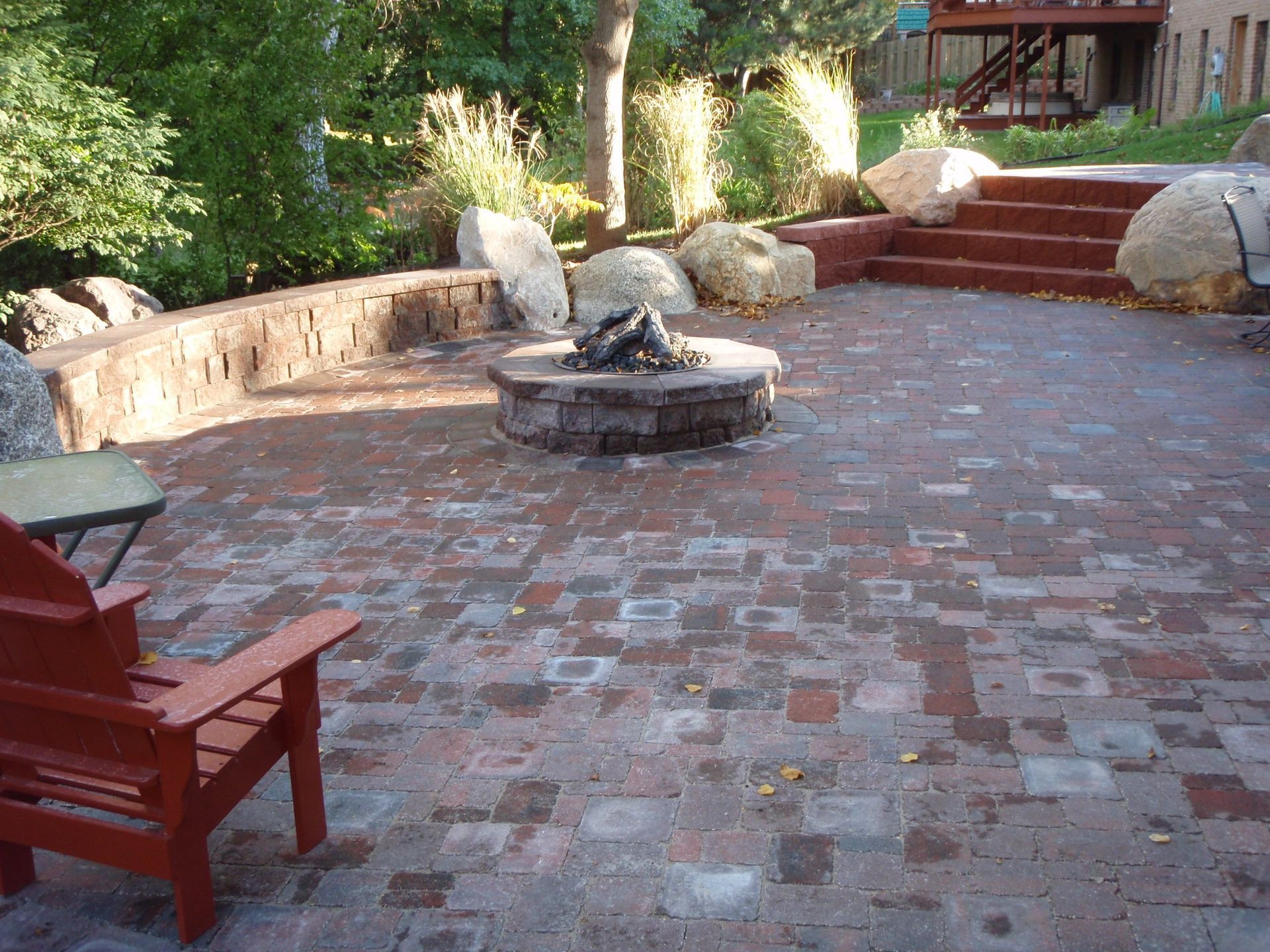 Brick patio with red bench, stone fountain, and steps leading to a garden area