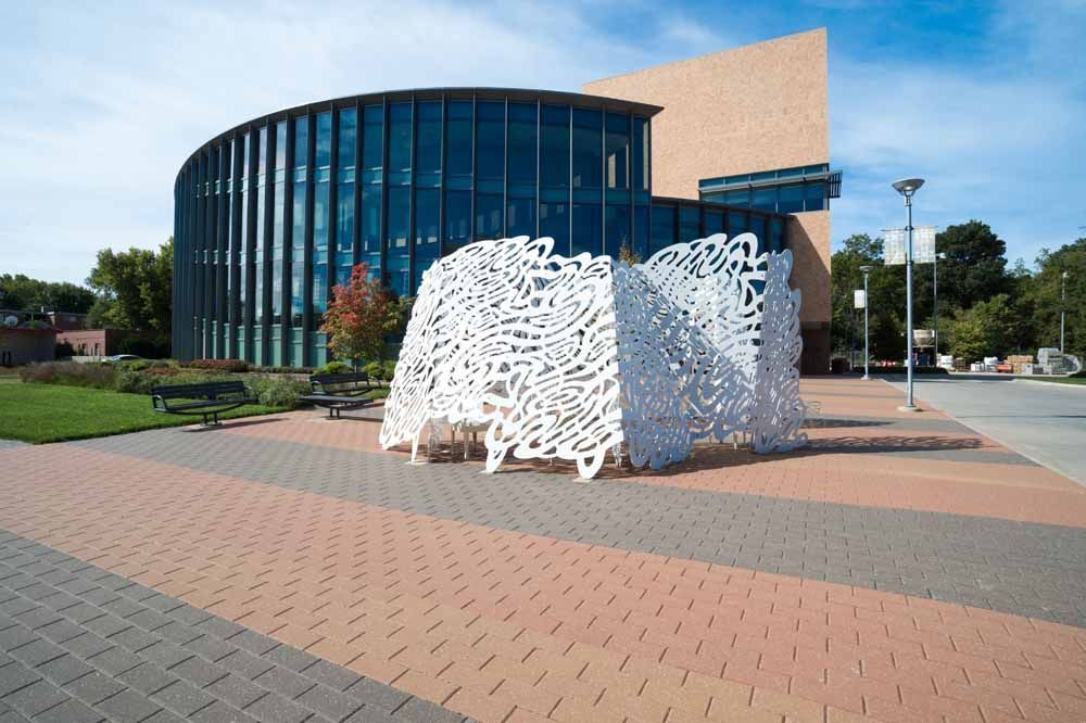 Modern glass building with a white abstract sculpture in a paved plaza