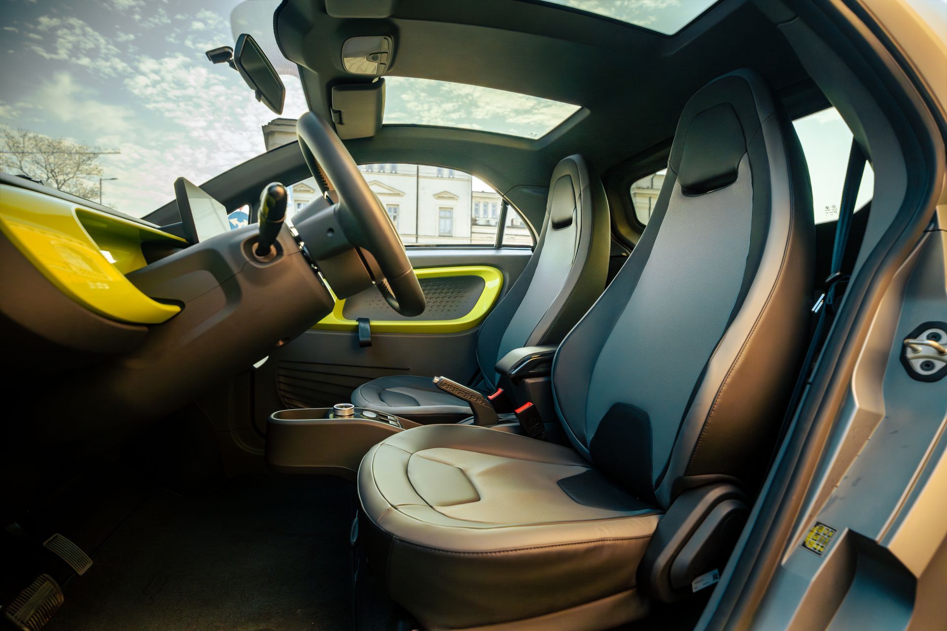 Modern car interior with tan and black seats, yellow accents, and large windows showing sky outside