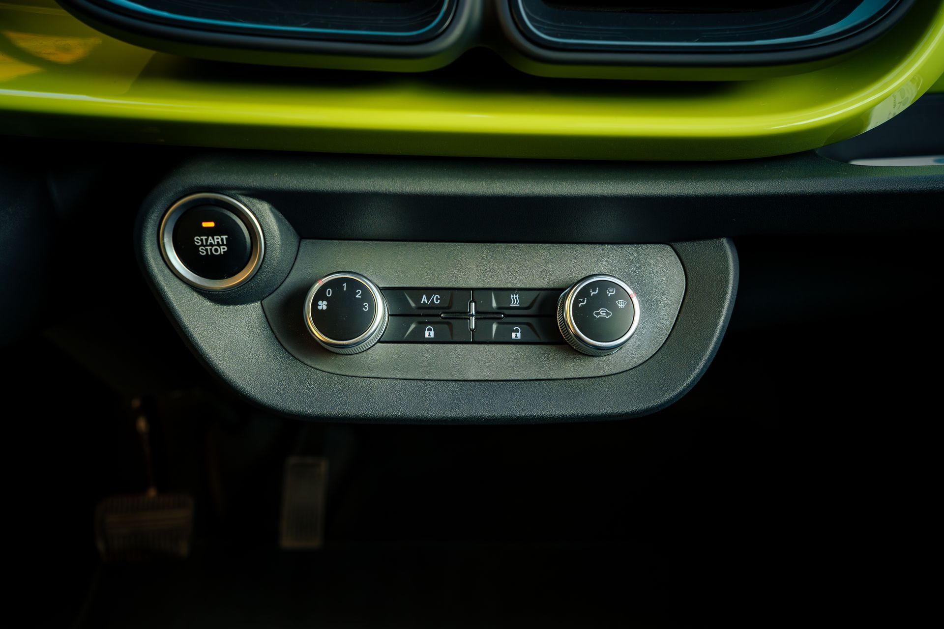 Car dashboard climate control panel with three rotary knobs and digital display, lit in green and silver.