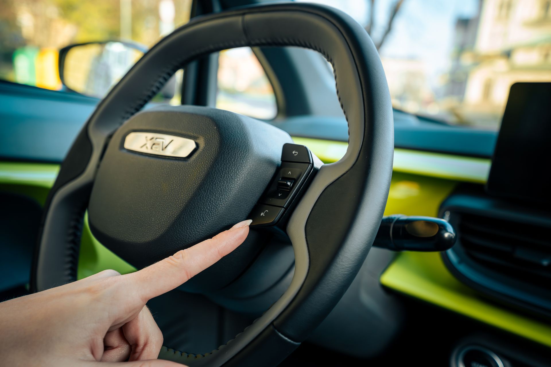 Finger pressing a button on a car steering wheel with a glowing dashboard in the background