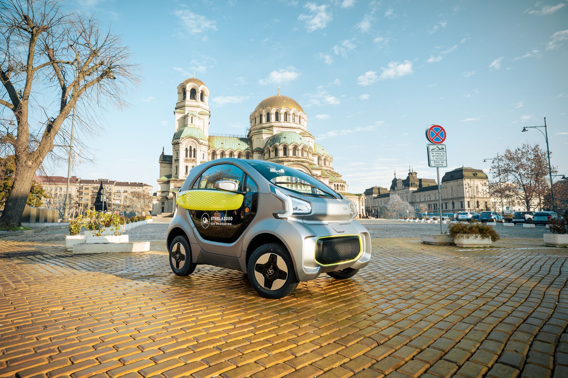 Small silver electric car on a cobblestone plaza with a cathedral in the background