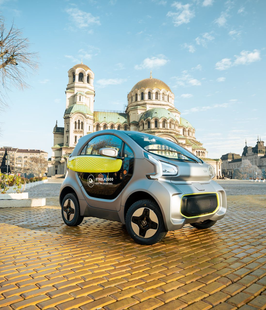 Compact futuristic car on a cobblestone plaza with a cathedral in the background under a blue sky