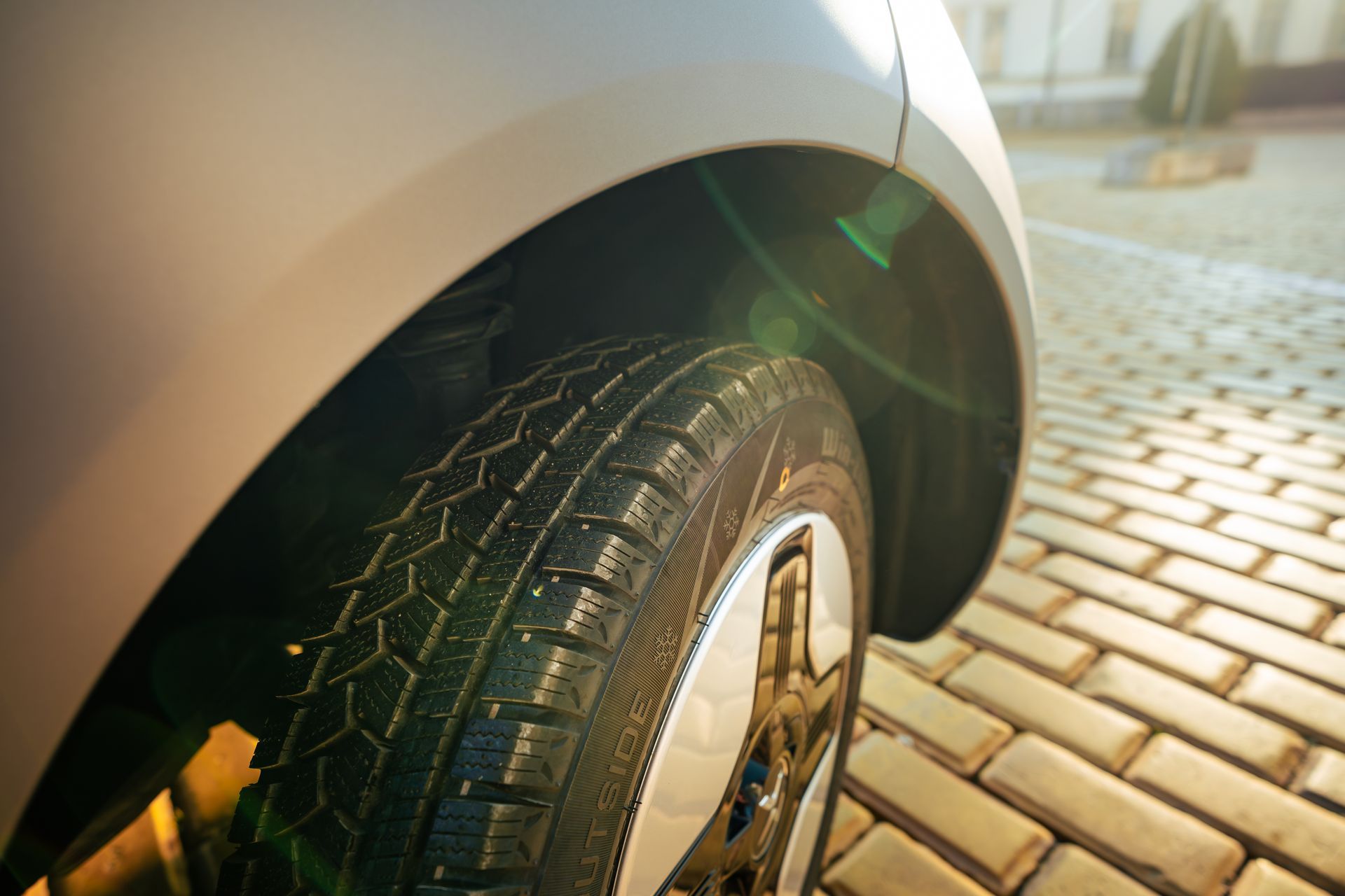 Close-up of a car tire and wheel on a sunlit brick driveway