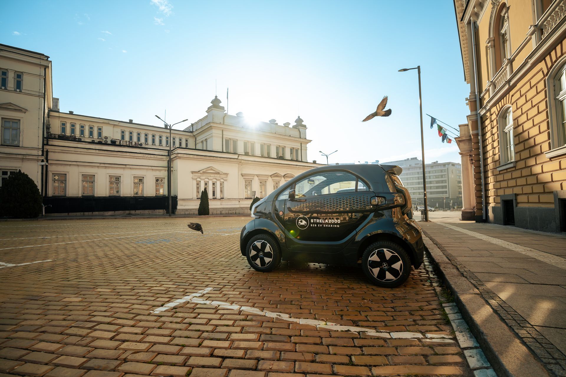 Small black electric car parked on a sunlit cobblestone street in a historic city square
