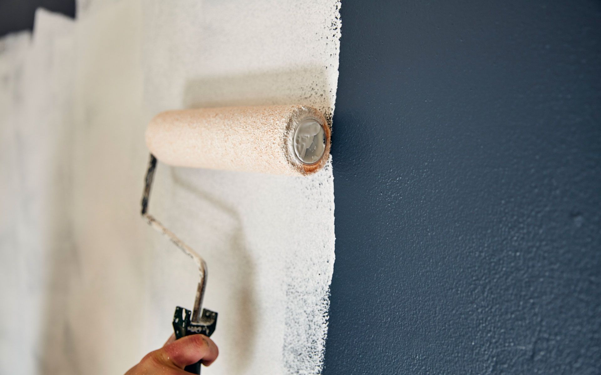 A person is painting a wall with a paint roller.