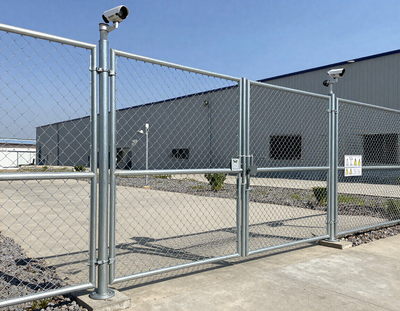 Chain-link security gate with a mounted camera in front of a gray industrial building.