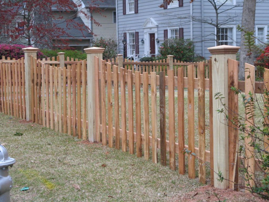 Wooden picket fence with brick pillars surrounding a grassy yard in front of a house