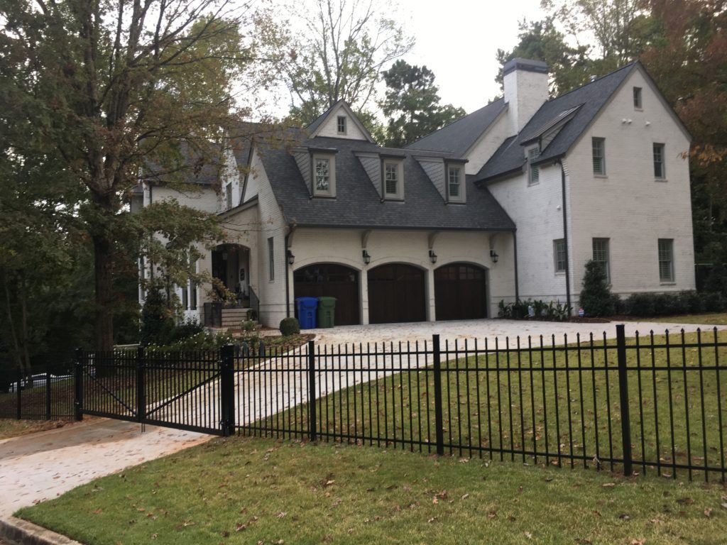 Large white house with dark roof, arched garage, and black metal fence along a driveway